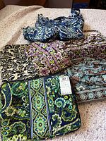 Top view of 7 Vera Bradley purses and bags in various colors and patterns on fabric surface.