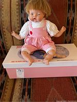 Full doll seated on original box, showing full outfit and box graphics
