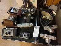 Overview of all 12 vintage cameras and accessories arranged on a tray, some cameras in leather cases, various styles visible