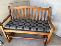 Front view of the wooden glider bench with cushion showing slatted back and armrests.