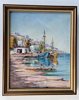 Framed oil painting showing coastal scene with boats and village, signed lower right, with visible minor crazing and frame wear.