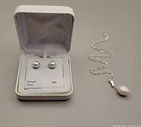Sterling silver pearl button earrings in their original white box with tag, and silver necklace with large pearl pendant placed beside the box on a neutral surface.