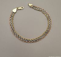 Bracelet laid out in a circle on neutral background showing tri-colour braided design and lobster clasp.