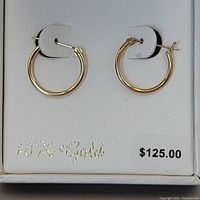 Photo showing the pair of small hoop earrings mounted on a white cardboard display inside a white box labeled '10K Gold' with a price tag $125.00.