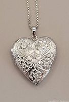 Close-up of the heart-shaped sterling silver locket showcasing the floral engraving and central small diamond.