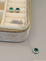 Sterling silver necklace with emerald-green cubic zirconia pendant and matching stud earrings displayed in a velvet box with compartments.