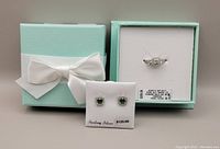 Jewelry set in original packaging with a blue box featuring a white bow. Ring displayed in the box with label showing size and price. Earrings mounted on white card labeled Sterling Silver $125.