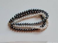 Three pearl bracelets (white and dark pearls) laid flat on white surface, showing length and size.