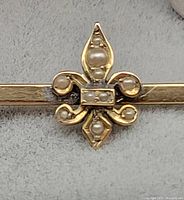 Close-up photo of the 14kt gold fleur-de-lis with embedded pearls and gold bar detail.