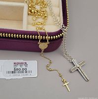 Photo showing both gold-plated rosary-inspired necklace with pendant, silver necklace with cross pendant set with stones, both laid near new purple velvet storage box. Price tag $80 for rosary-inspired necklace visible.