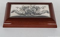 Front angled view of the jewelry box showing the polished solid oak wood frame and detailed sterling silver lid with fruits and foliage design.