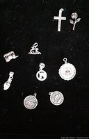 Top view showing all seven sterling silver pendants on a black background, including cross, rose, hand, architectural building, and circular pendants with different motifs.