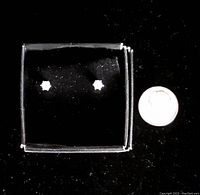 Pair of diamond stud earrings displayed in black box with coin for scale