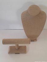 Beige fabric-covered jewelry necklace bust and matching bracelet display stand photographed against plain backdrop.