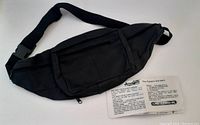 Black genuine leather concealed carry waist pouch with adjustable strap, plastic buckle, and front pocket with zipper. Includes a paper insert confirming product information.