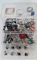 Top view of 4-drawer acrylic jewelry organizer filled with assorted costume jewelry pieces, including bracelets, rings, necklaces, and earrings.