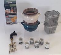 Front view of soup/chowder bowls stacked, shot glasses lined in front, wooden horse head wine opener to left, and two plastic berry containers stacked to right.