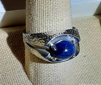 Side angle showing hammered texture on sterling silver band and prong setting holding oval blue stone.