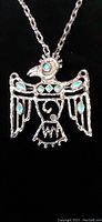 Close-up of silver Thunderbird pendant with turquoise-colored stones set in the wings and head, showing intricate design and a missing turquoise stone.