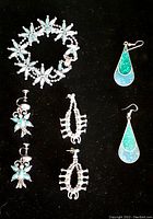 Top-down view of a turquoise and silver bracelet with floral design and three pairs of earrings on black background