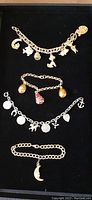 Four vintage charm bracelets displayed vertically on dark background showing individual charms and chain types.