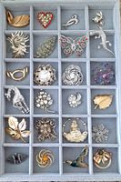 Full view of vintage lot 24 brooches in a gray partitioned display tray showing overall assortment and condition.