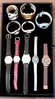 Lot of 10 watches in single display case; variety of bands and dial styles visible.