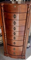 Full frontal view of wooden jewelry box showing 8 drawers with metal ring pull handles and decorative side columns, top drawer with keyhole