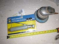 Photo of packaged Power Fist Deadman Sandblasting Gun and old palm sander or polisher attachment with measuring tape showing size approximately 8 inches.