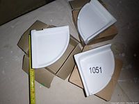 Photo showing three white ceramic quarter-circle soap holders, arranged on cardboard boxes. A measuring tape next to one soap holder shows approximately 8 inches in length on each side.