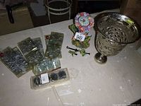 Photo showing unopened Christmas decoration packages, floral clock with flowers around clock face, and metal vase.