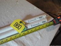 Close-up photo showing two white curtain rod sections in original plastic packaging with IKEA labels and tape measure indicating length about 36-40 inches for each section.
