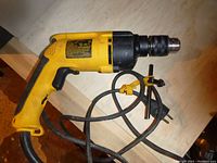Yellow DeWalt hammer drill laid flat showing the side with label and chuck key tied to the cord.