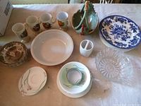 Top view of assorted dishes on a beige surface including mugs, plates, a glass dish, and a decorative basket-shaped dish.
