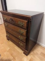 Brown wooden dresser with carved shell motif and brass handles missing one handle.