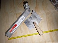 Two drywall tools on a wooden surface with a measuring tape for scale: a Goldblatt corner crimper and a Marshalltown corner trowel with a worn wooden handle, both showing drywall residue.