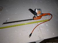 Side angle of Black & Decker hedge trimmer showing blade length and body detail with orange power cable.