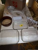 Kitchen bowls and baking trays arranged on a table showing clear glass rectangular baking trays, various ceramic bowls and baking dishes, and metal muffin tray.