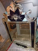 Front view of mirror showing decorative glass frame with etched floral motif and scalloped crest.