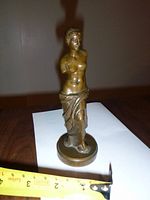 Front view of metal Venus De Milo figurine with tape measure showing width around 2.5 inches