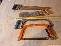 All four saws laid on a wooden surface showing condition and size relative to a measuring tape