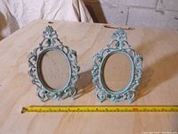 Two ornate metal photo frames displayed side by side on a wooden surface with a measuring tape showing approx. 10 inches height
