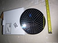 Photo of top side of round chrome rain shower head showing nozzles and approximate diameter with measuring tape