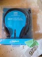 Photo of one Logitech H111 stereo headset in unopened packaging, showing front with microphone boom and 3.5mm jack.