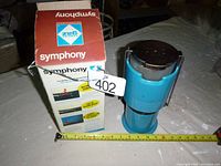 Photo showing blue Symphony gas lamp next to its original box with measuring tape indicating size.