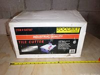Closed original box of Toolway tile cutter with label showing model OATS07, features and industrial quality branding.