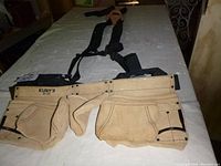 Full view of Kunys apron and suspenders laid flat showing apron's multiple tool pockets and suspenders' straps.