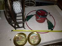 Photo showing red metal Christmas tree stand with green tree decorations, brass plate frames with glass featuring scenic prints, and part of the metal magazine rack.