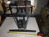 Photo of black metal TV mount laying flat, showing the horizontal mounting bar with integrated level bubbles and adjustable vertical arms.