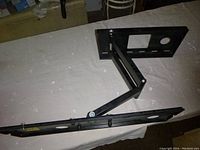 Side view of black articulating TV wall bracket showing arm and mounting plate on a white surface.
